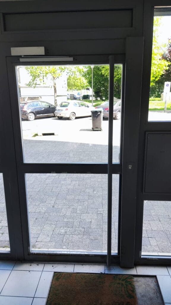 Réglage de porte d'entrée vitrée à Mulhouse – Intervention technique Réglage d'une porte vitrée d'entrée d'immeuble avec vue extérieure sur parking à Mulhouse